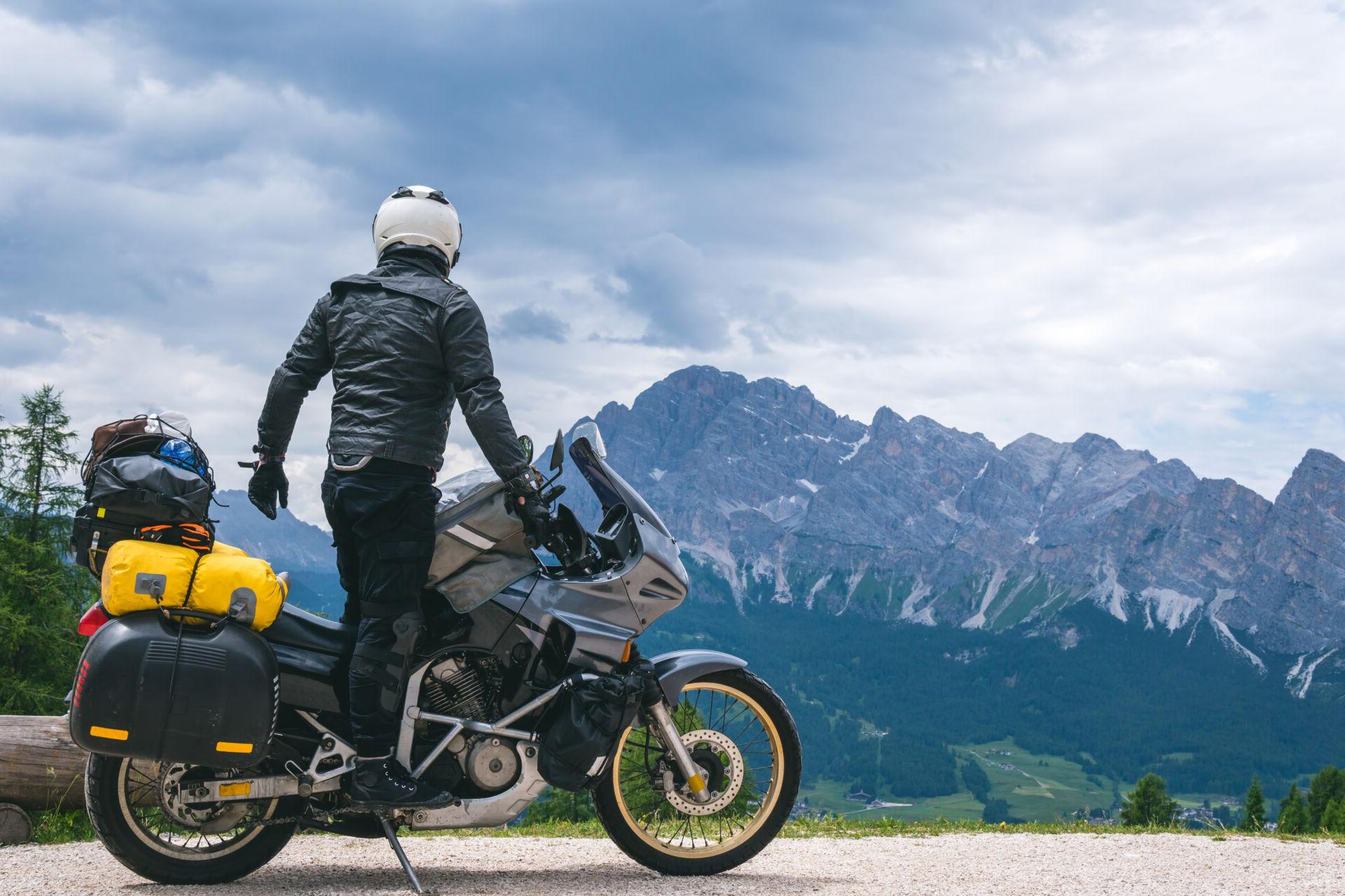 A motorcyclist takes a pit stop to take in beautiful mountain scenery.